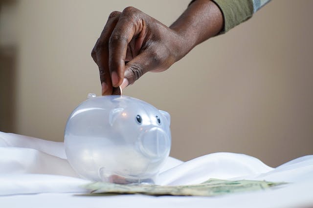 person putting coins in a clear piggy bank